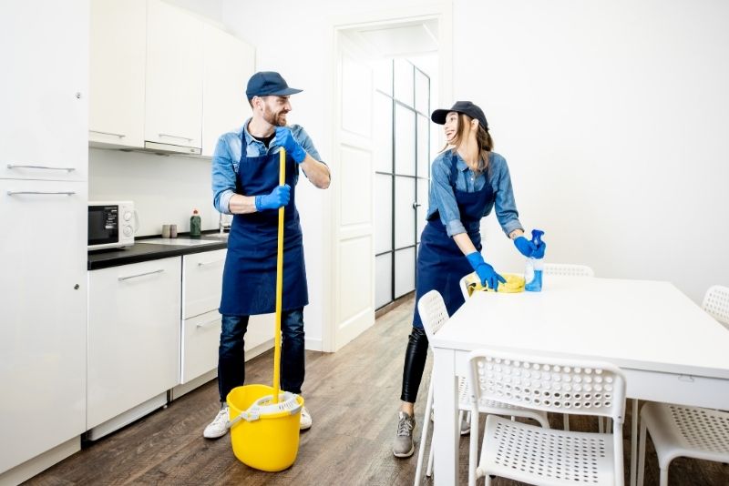 A couple of Cleaners from Cairns Company working in a kitchen. The man is mopping the floor and the woman is wiping a table.