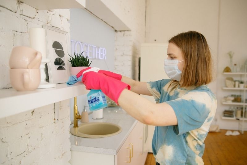 Masked cleaner wiping down a kitchen shelf and counter