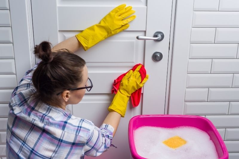Cleaner wiping down a door with a bucket of soapy water
