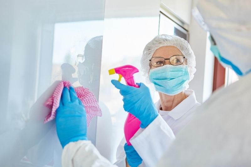 Two masked cleaners wiping down a glass surface during a deep clean