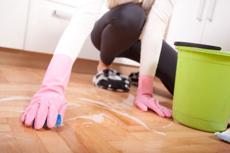 Cleaner in gloves scrubbing a timber floor by hand
