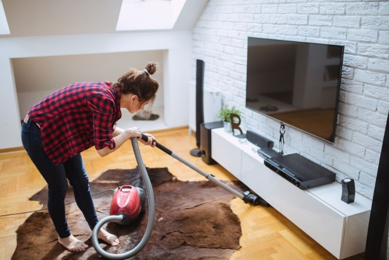 Cleaner vacuuming a rug in front of a TV unit