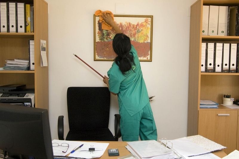 Cleaner dusting a wall-mounted picture frame in an office